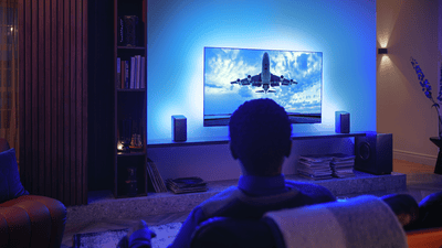 Muškarac uživa u svom Philips Ambilight TV-u povezanom s Wi-Fi zvučnicima