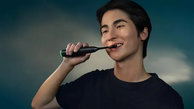 A young man smiles as he brushes his teeth with a Philips Next-Generation DiamondClean electric toothbrush.