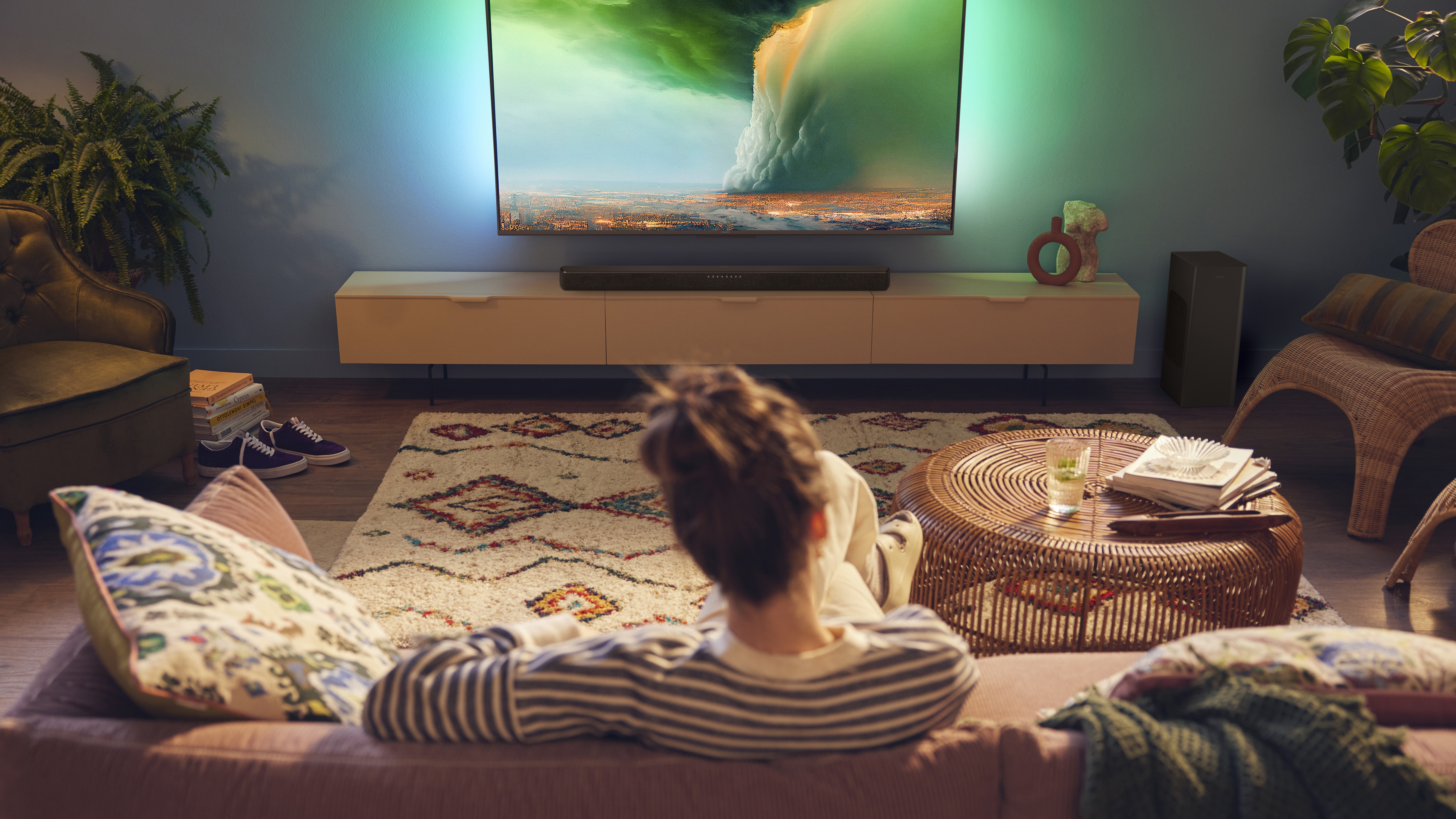 Person watching Philips Ambilight TV with a soundbar in a cozy living room
