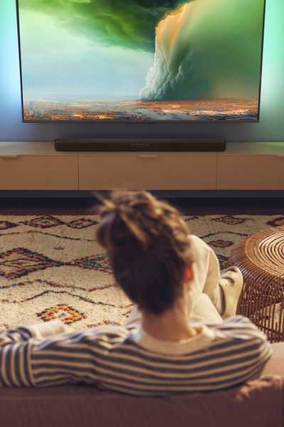Person watching Philips Ambilight TV with a soundbar in a cozy living room