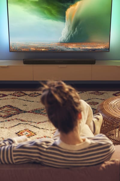 Person watching Philips Ambilight TV with a soundbar in a cozy living room