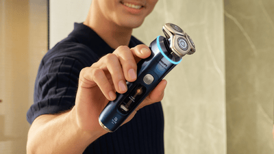 A close-up of a man in a navy shirt showing off his Philips i9000 Prestige Ultra electric shaver.
