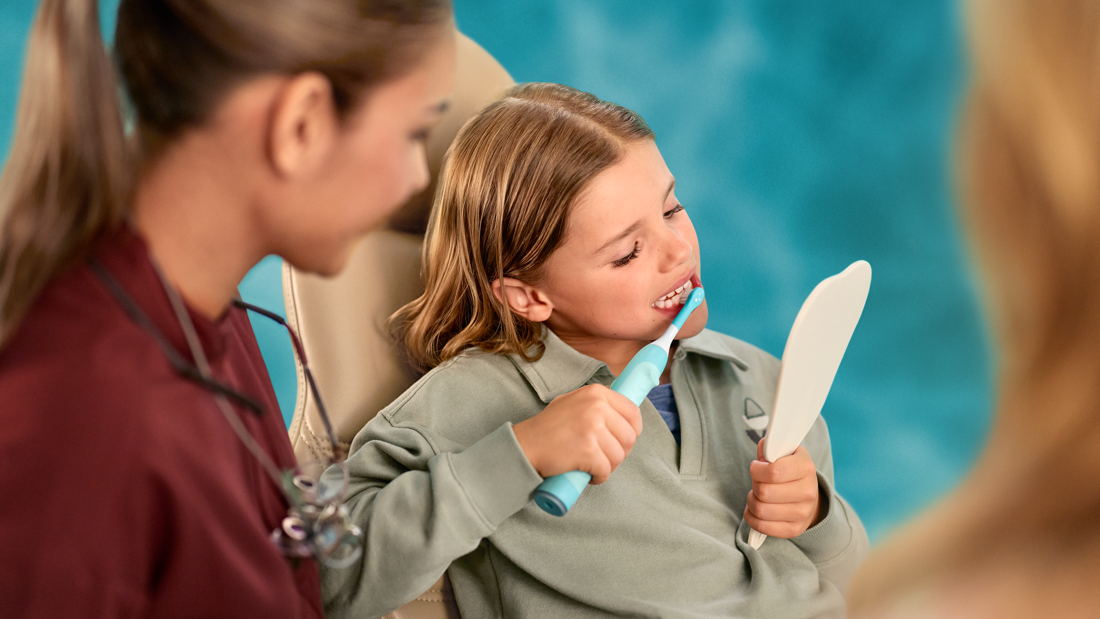 Tandheelkundige professional die kijkt hoe een kind een elektrische Sonicare For Kids-tandenborstel gebruikt.