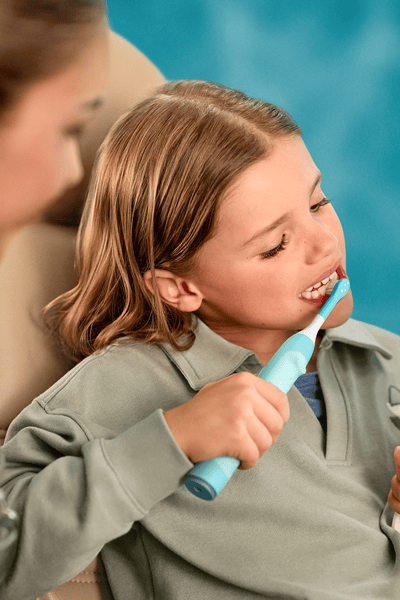 Tandheelkundige professional die kijkt hoe een kind een elektrische Sonicare For Kids-tandenborstel gebruikt.