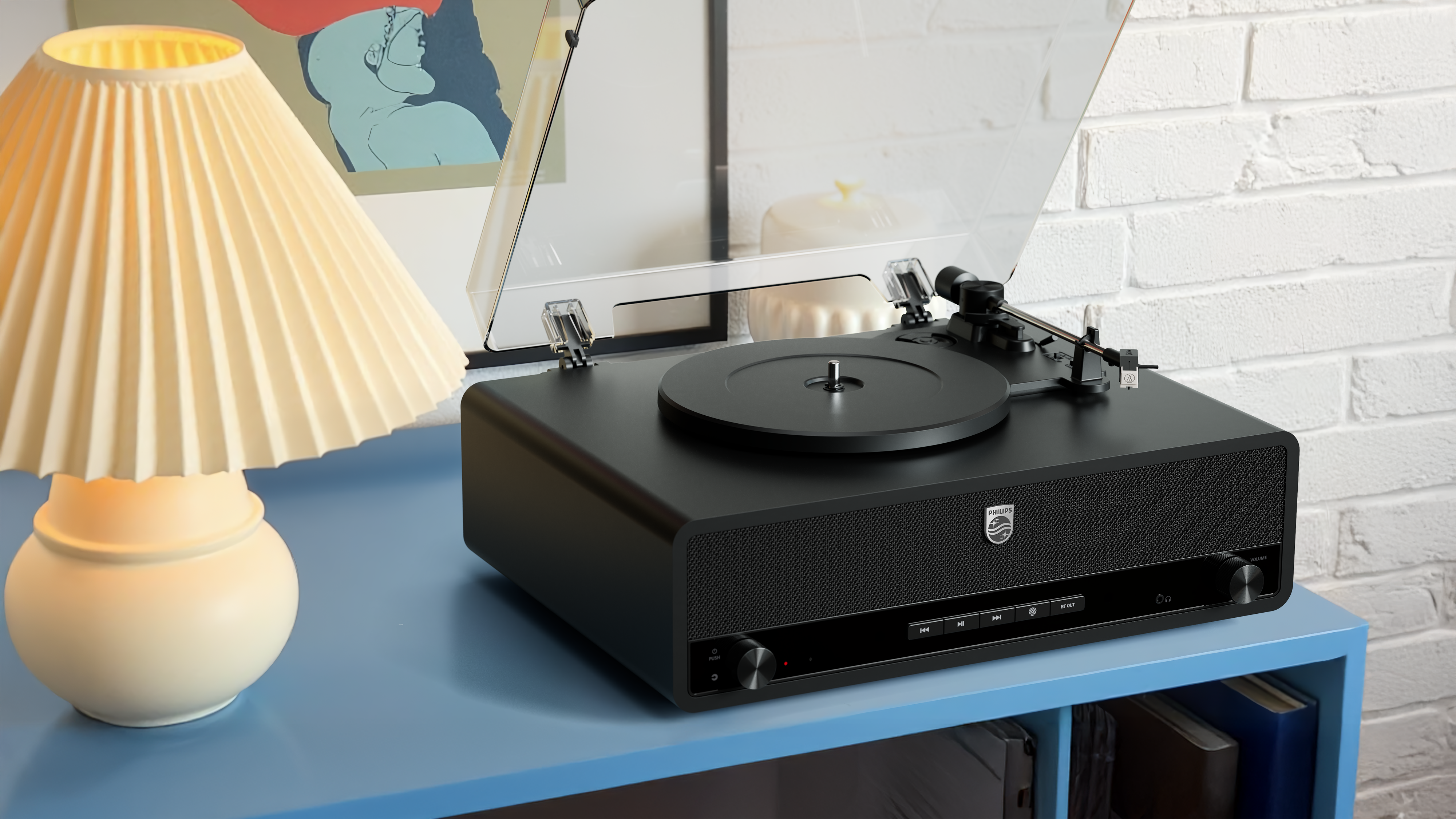 Eleganten črn gramofon Philips je postavljen na modri mizi v sodobnem domačem okolju, poleg mehko sijoče namizne svetilke. Ustvarja toplo in vabljivo izkušnjo zvoka.