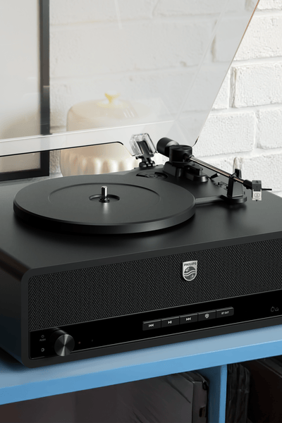 Eleganten črn gramofon Philips je postavljen na modri mizi v sodobnem domačem okolju, poleg mehko sijoče namizne svetilke. Ustvarja toplo in vabljivo izkušnjo zvoka.