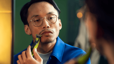 A man is using a Philips OneBlade to shave his beard to avoid dry skin after shaving.