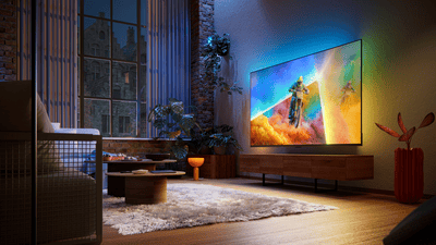 Philips Ambilight TV in a contemporary living room, displaying a motocross racing scene with colorful ambient lighting extending beyond the screen and illuminating the surrounding wall.Philips Ambilight TV in a contemporary living room, displaying a motocross racing scene with colorful ambient lighting extending beyond the screen and illuminating the surrounding wall.