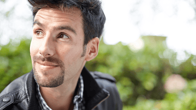 A man sporting a fashionable beard looks off into the distance in an outdoor setting.