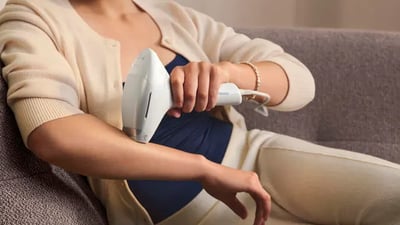 A close-up of a woman using the Philips Lumea 9900 Pro IPL device on her arm hair.