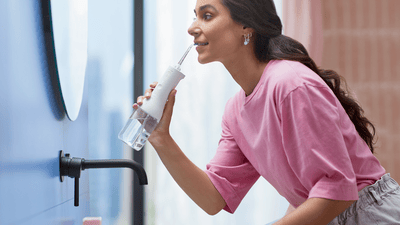 A woman is using a Philips Air Flosser in front of her bathroom mirror.