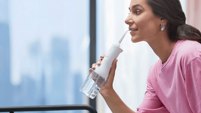 A woman is facing to the left flossing her white teeth with the Philips Sonicare Power Flosser.