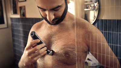 A man uses a Philips electric shaver to remove his chest hair.