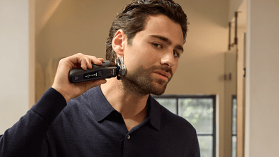 Un uomo in camicia nera si rade la barba con un rasoio Philips nero.