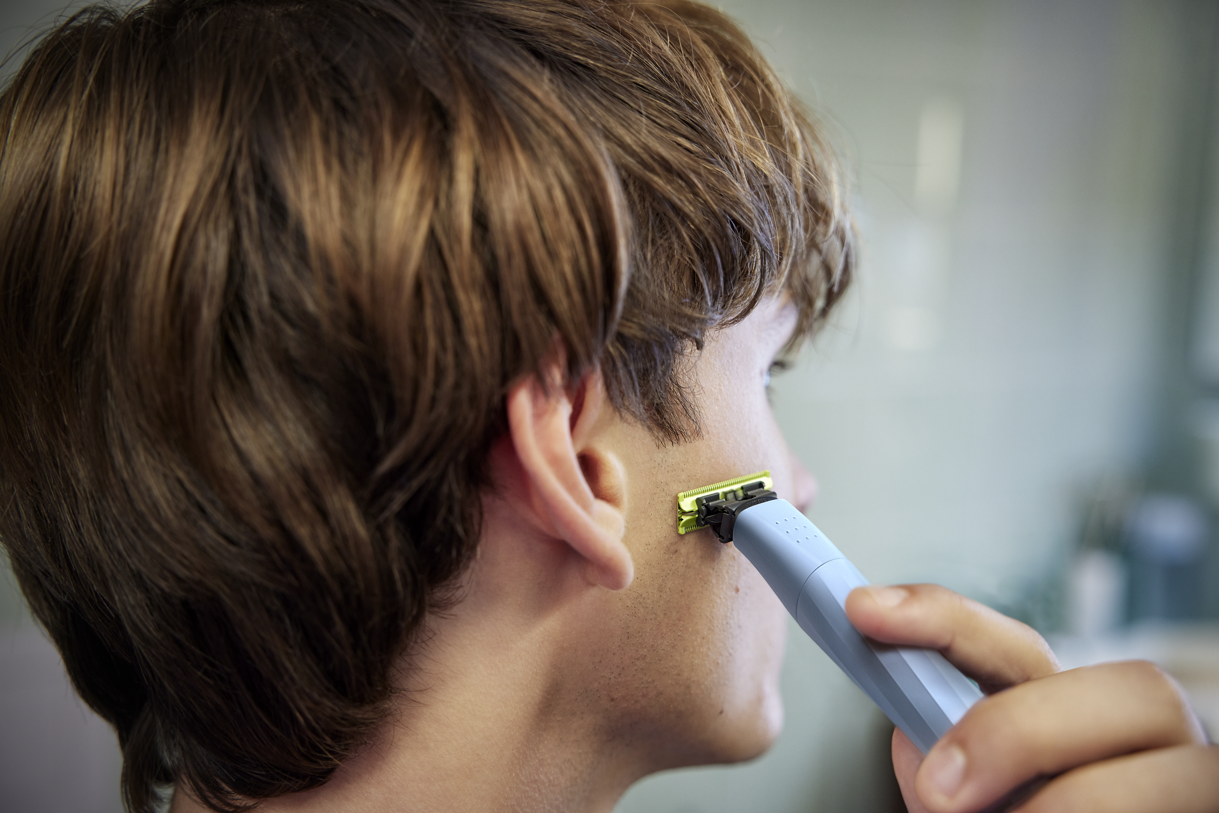 Un giovane distoglie lo sguardo dalla telecamera mentre si rade le basette con un Philips OneBlade.