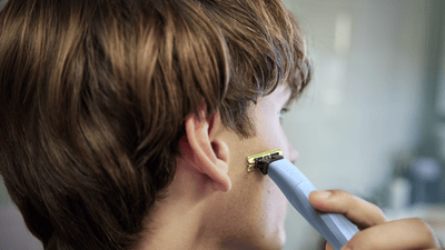 A young man looks away from the camera as he shaves his sideburns with a Philips OneBlade.