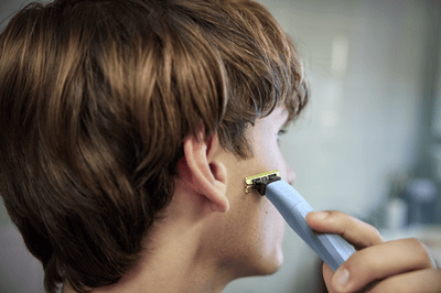 A young man looks away from the camera as he shaves his sideburns with a Philips OneBlade.