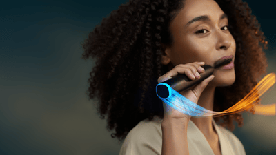 Uma mulher de cabelo encaracolado escova os dentes com uma escova elétrica Philips Next-Generation DiamondClean.