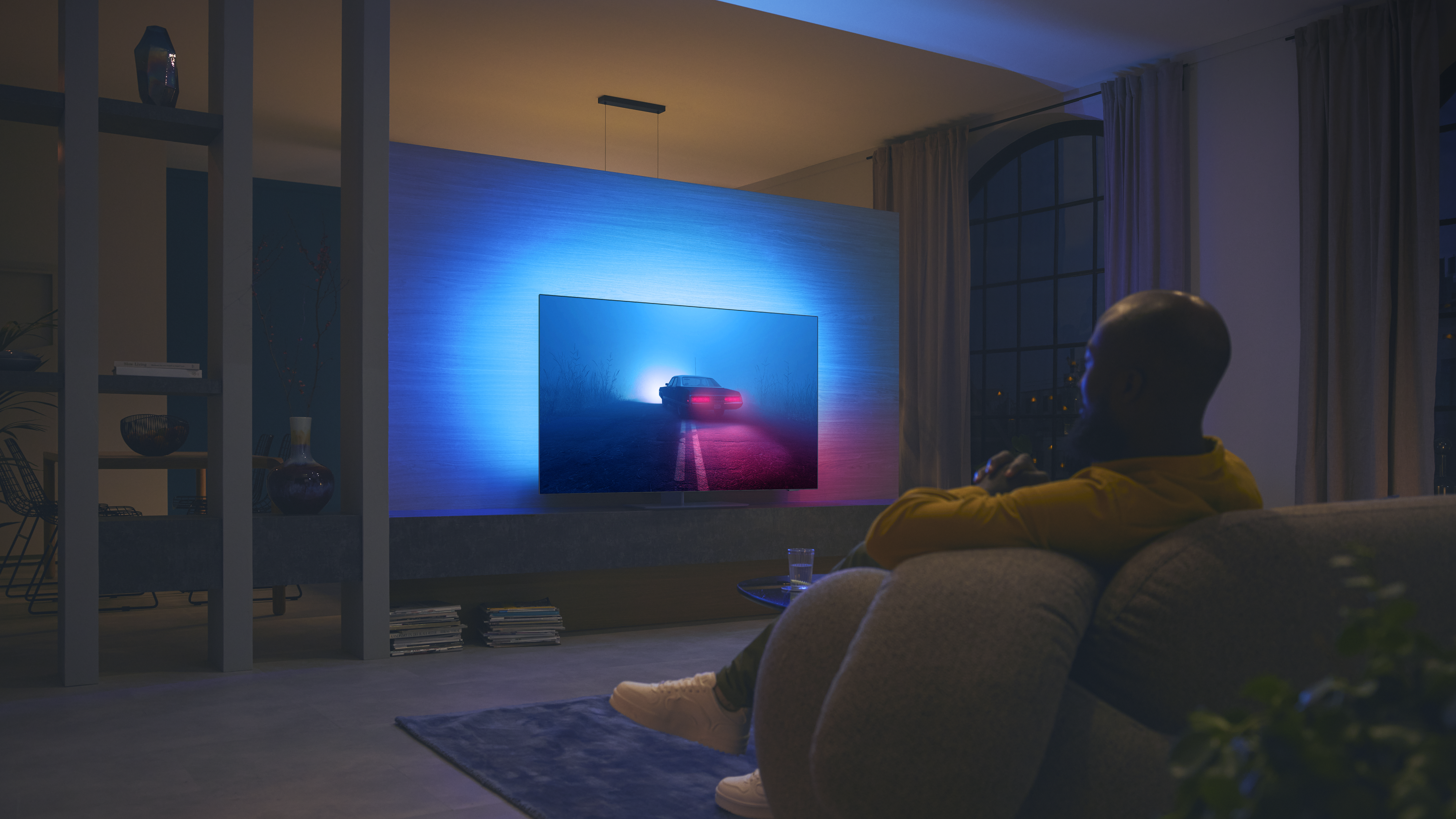 Άτομο που παρακολουθεί τηλεόραση Philips Ambilight, με μπλε και κόκκινο ατμοσφαιρικό φωτισμό στον τοίχο.