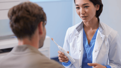 A female dental professional is giving a man advice on gingivitis and inflamed gums while holding a Philips electric toothbrush in her hand.