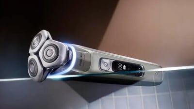 A Philips i9000 Prestige Ultra electric shaver sits on the edge of a clear bathroom table.