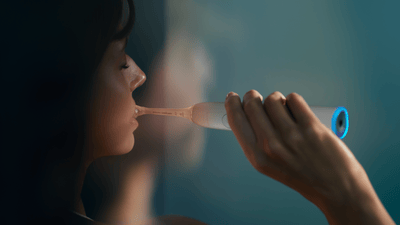 A young woman with dark hair, in a green robe, brushes her teeth with a Philips electric toothbrush.
