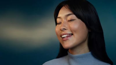 A young woman smiles as she licks her white teeth against a dark gradient background.