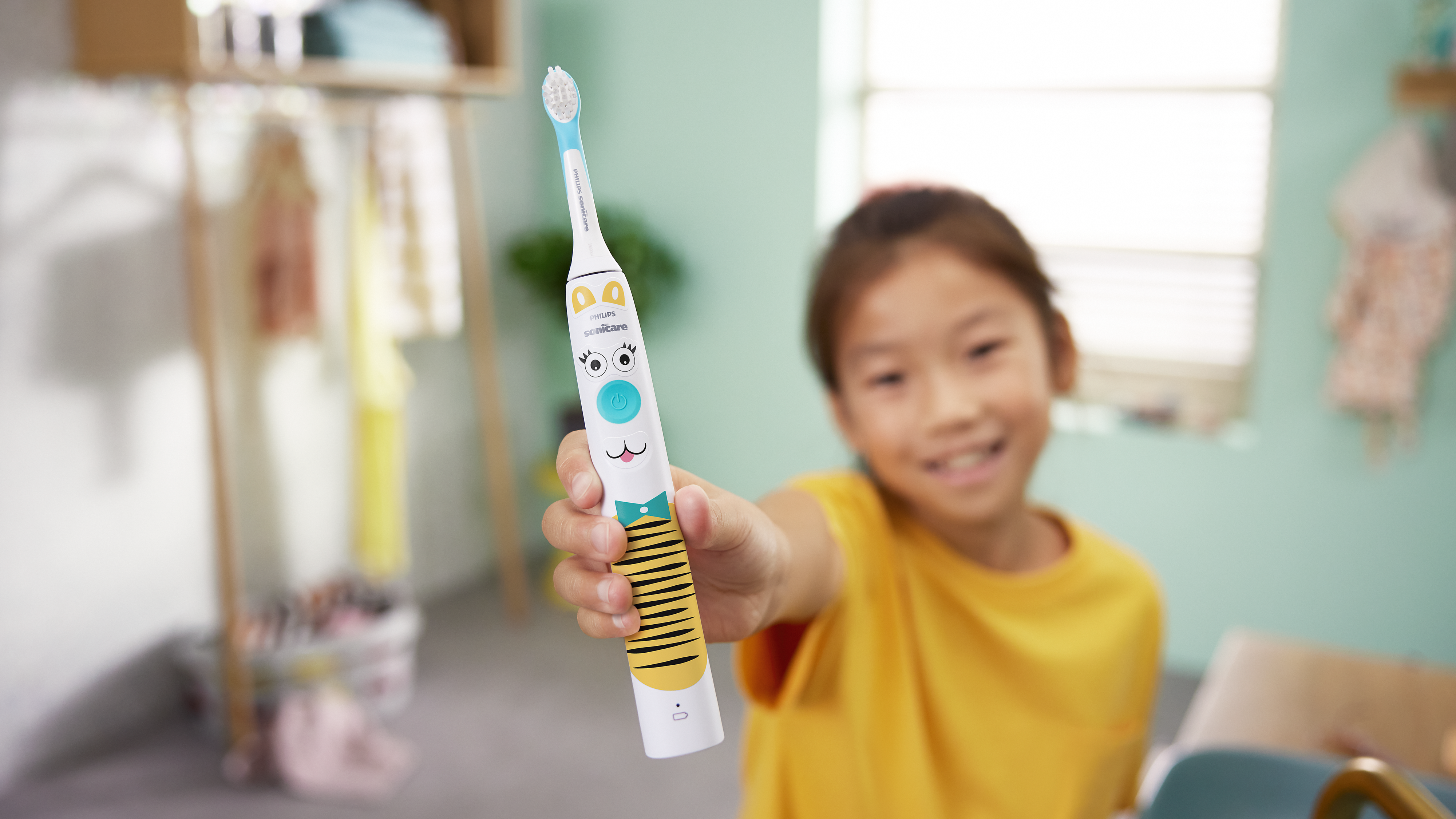 A young child wearing yellow holds their Philips kids electric toothbrush up proudly to the camera.