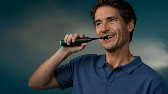 A middle-aged man brushes his teeth using a Philips Next-Generation DiamondClean electric toothbrush.