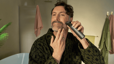 A man using a Philips trimmer in front of a mirror to prep his facial hair for a pencil moustache.