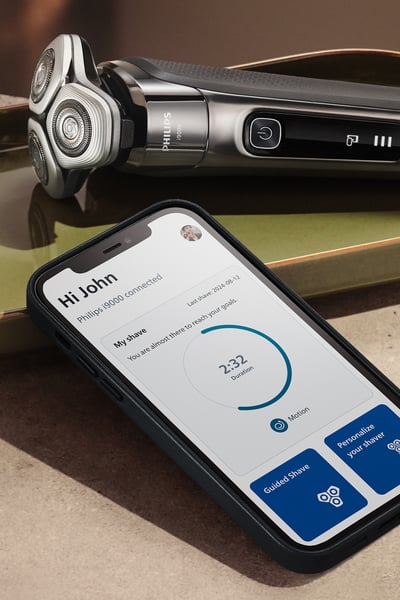 Una mano che tiene un rasoio e accanto ad esso un display dell'app Male Grooming.
