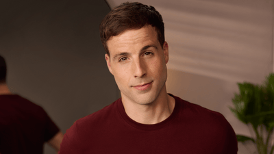 A man with no beard wearing a maroon t-shirt looks directly at the camera with a slight grin.