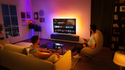 Dwóch mężczyzn ogląda telewizję Ambilight zamontowaną na ścianie w salonie