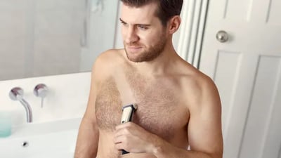 A man uses a Philips Body Groomer 7000 Series to shave his hairy chest.
