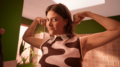 A woman in a bathroom is showing off her arm muscles while making a funny face.