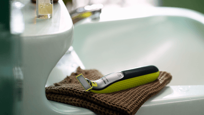 A Philips OneBlade 360 sits by a bathroom sink.