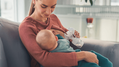 Madre amamantando a su bebé y el otro lado usando un extractor de leche eléctrico