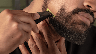 A close-up picture of a man's face capturing him shaving his beard into a Henriquatre using a Philips OneBlade.