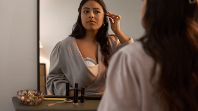 A woman, wearing her Philips Avent Wearable Breast Pump, looks at herself in a mirror.