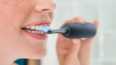 A young woman is using a Philips electric toothbrush with a sensitive brush head to avoid bleeding gums.