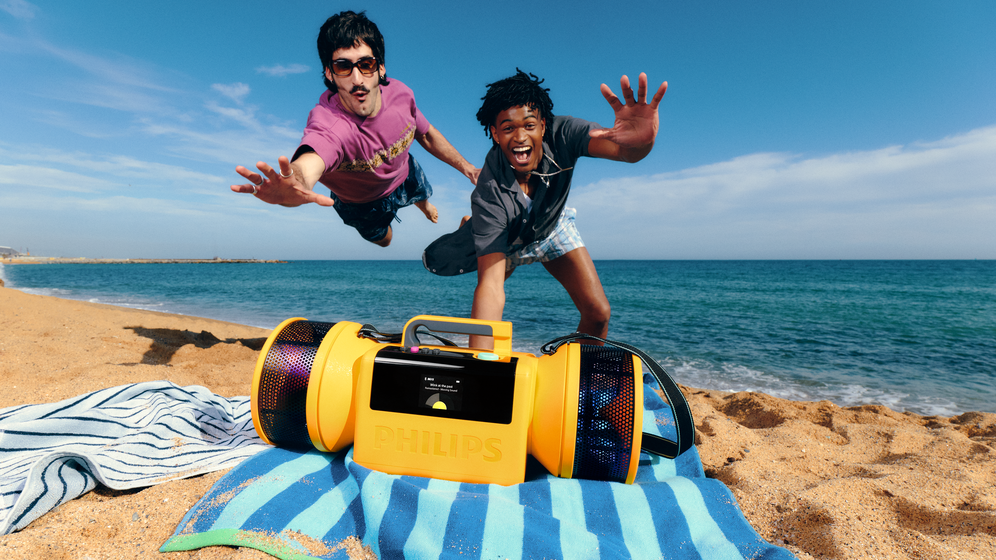 Zwei Männer, die an einem sonnigen Strand über einem gelben tragbaren Lautsprecher au