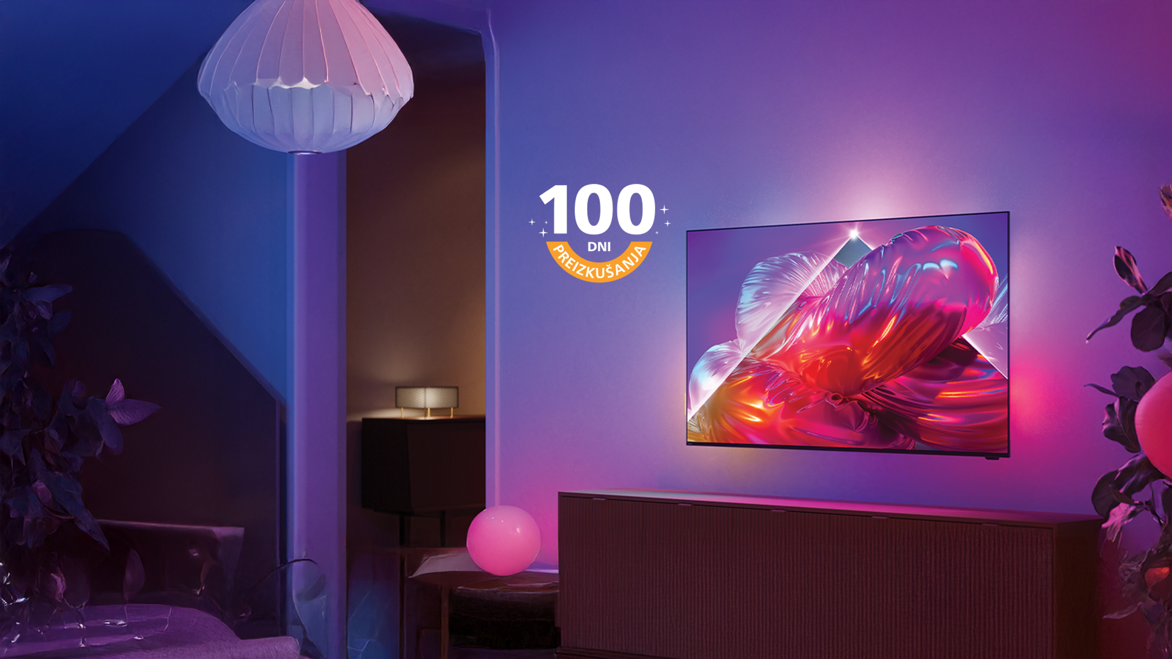 Televizor Philips Ambilight, nameščen na steni dnevne sobe, prikazuje živahno rožnato umetniško podobo, medtem ko za zaslonom sveti barvita ambientalna osvetlitev.