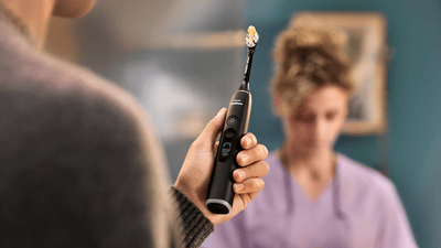 Un homme tient une brosse électrique Philips DiamondClean dans ses mains et son dentiste travaille derrière lui.