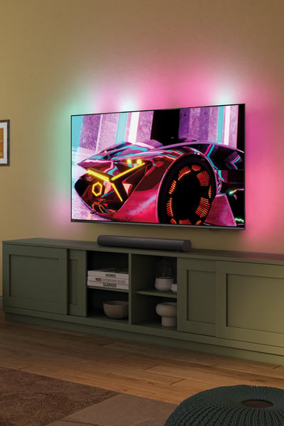 A person relaxes in front of an Ambilight TV, with a soundbar below