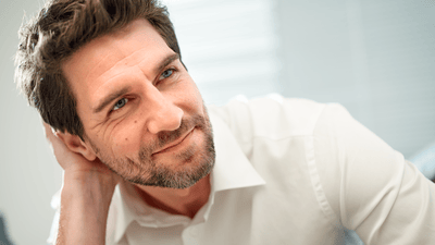 Frontal image of a man in a white shirt looking towards the camera letting his beard grow to achieve a Viking beard.