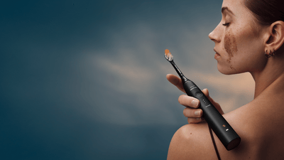 A young woman seen from the back, her head is tilted, and she’s holding a black Philips Sonicare toothbrush over her shoulder.