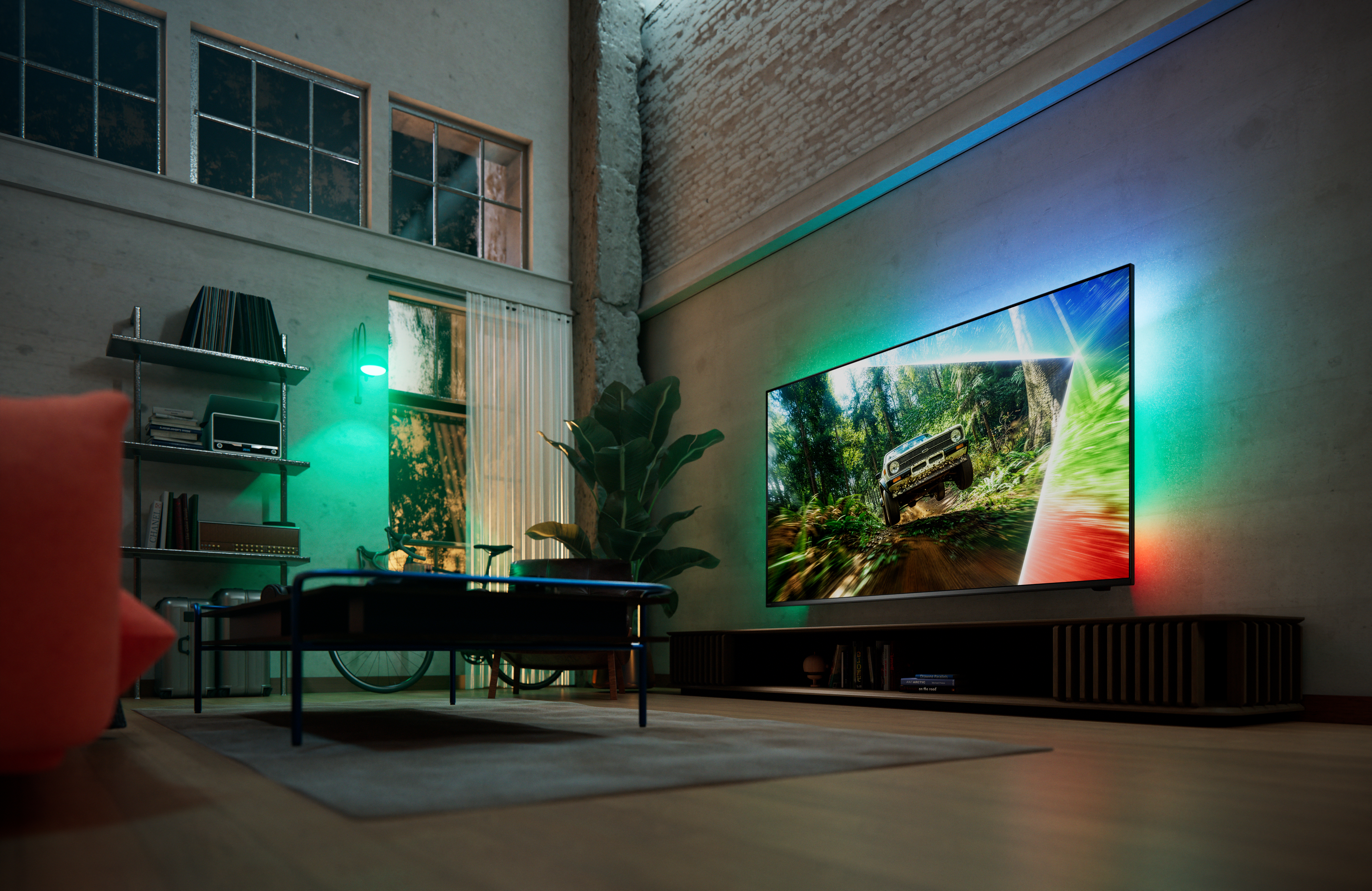 Philips Ambilight TV in a contemporary loft living room, displaying an off-road racing scene with colorful ambient light extending beyond the screen onto the surrounding wall.