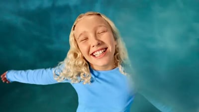 A child smiles widely as she stands with her arms outstretched.