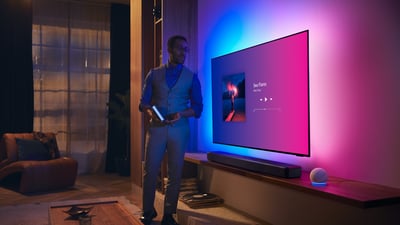 Persoon in een moderne woonkamer bij een Philips Ambilight-tv met muziekinterface en Fidelio-soundbar