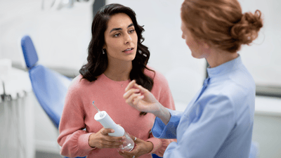 A woman in a pink top is consulting a female dental professional about how to fix bad breath, holding a Philips Air Flosser in her hand.
